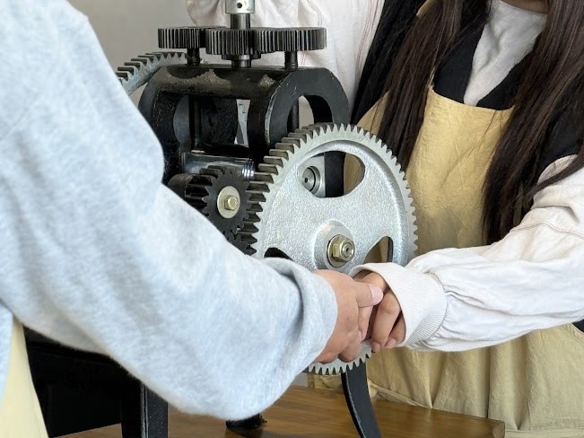 太田市の指輪工房にある本格的な彫金機材（ローラー）を使い、二人で結婚指輪のプラチナを伸ばす共同作業の風景